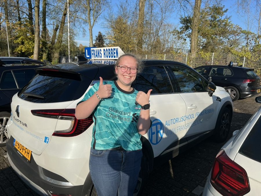Geslaagde leerling met duimen omhoog bij de witte Renault Captur