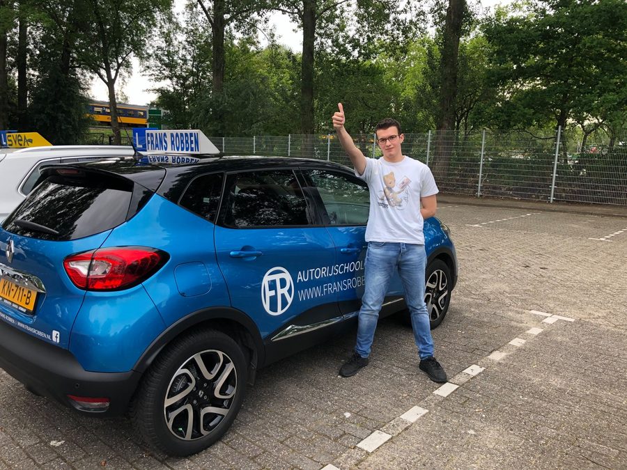 Geslaagde leerling met duim omhoog bij de blauwe lesauto