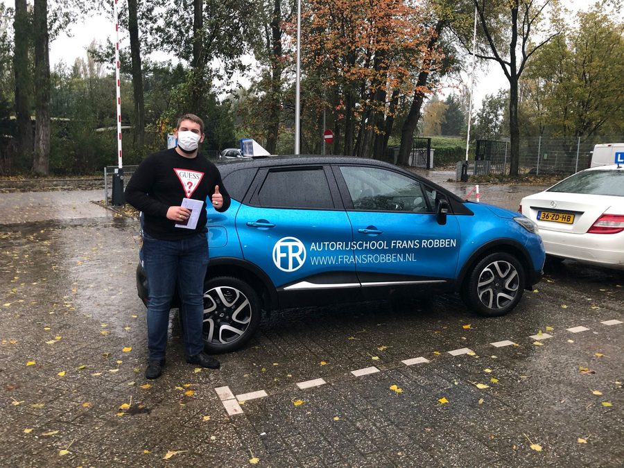 Geslaagde leerling met duim omhoog naast de lesauto
